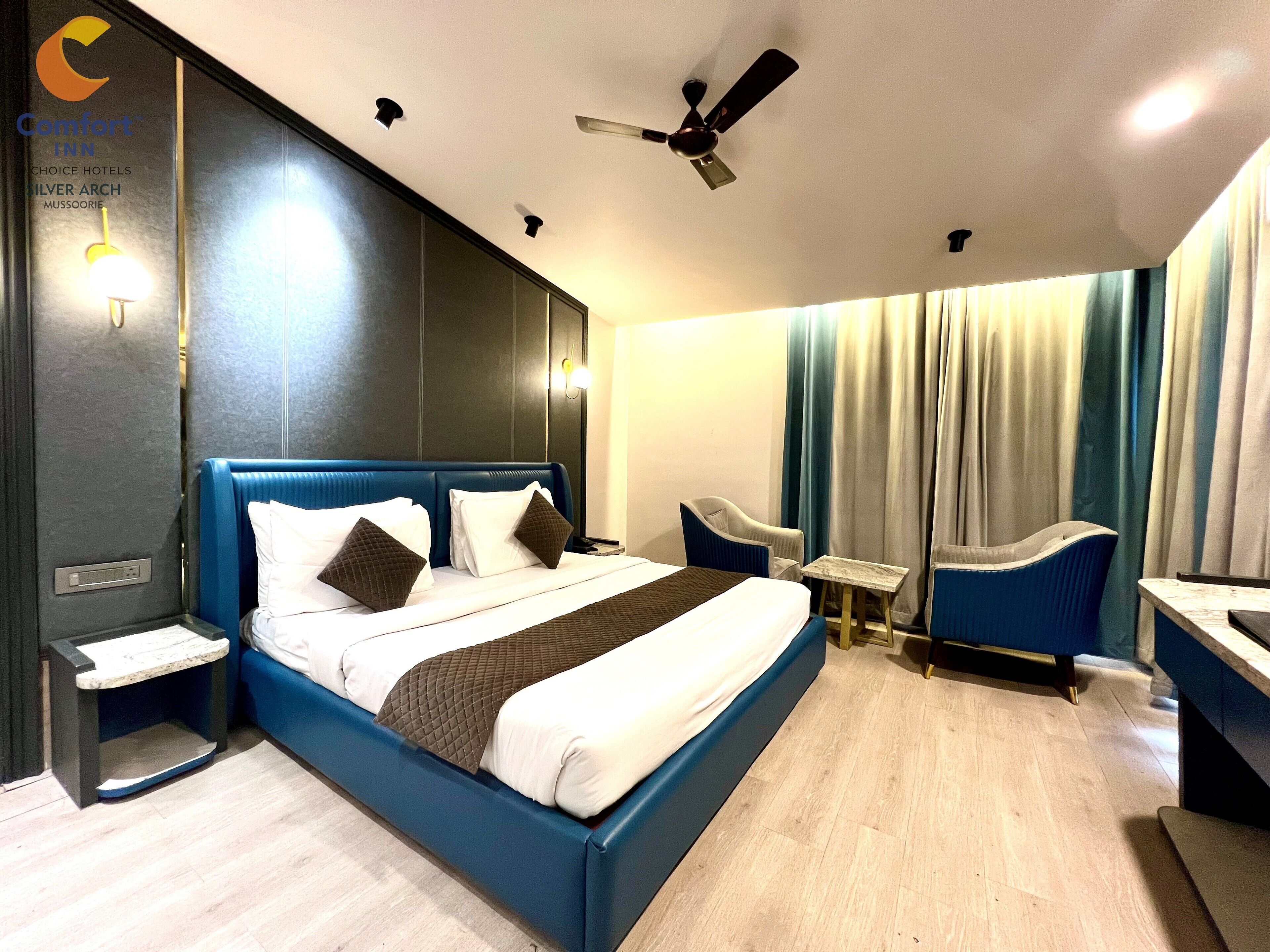 A modern hotel room with a large bed, a desk, a chair, and a ceiling fan.