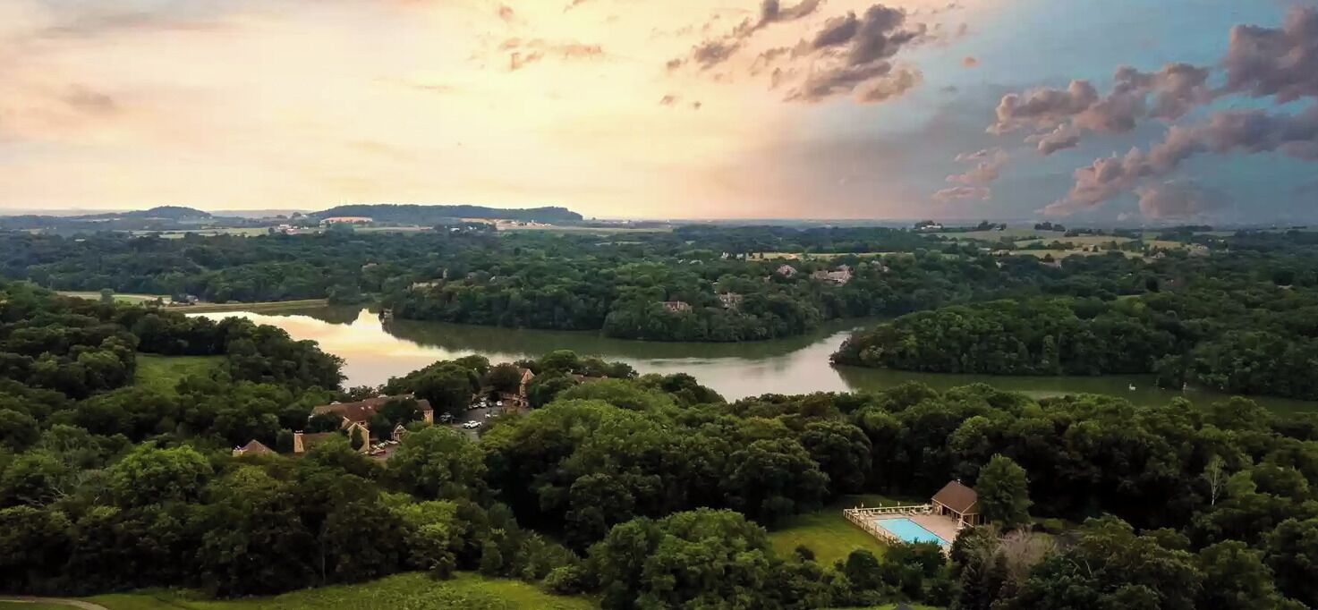 Um imóvel à beira do lago com piscina, rodeado por vegetação densa e vista distante para colinas.
