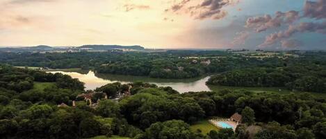 Um imóvel à beira do lago com piscina, rodeado por vegetação densa e vista distante para colinas.