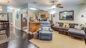 A modern living room with a blue recliner, a gray sofa, and a kitchen area with wooden cabinets and a microwave. - Luxurious King bed Condo across from Beach, Boardwalk, Shops and Restaurants.  (Biloxi)