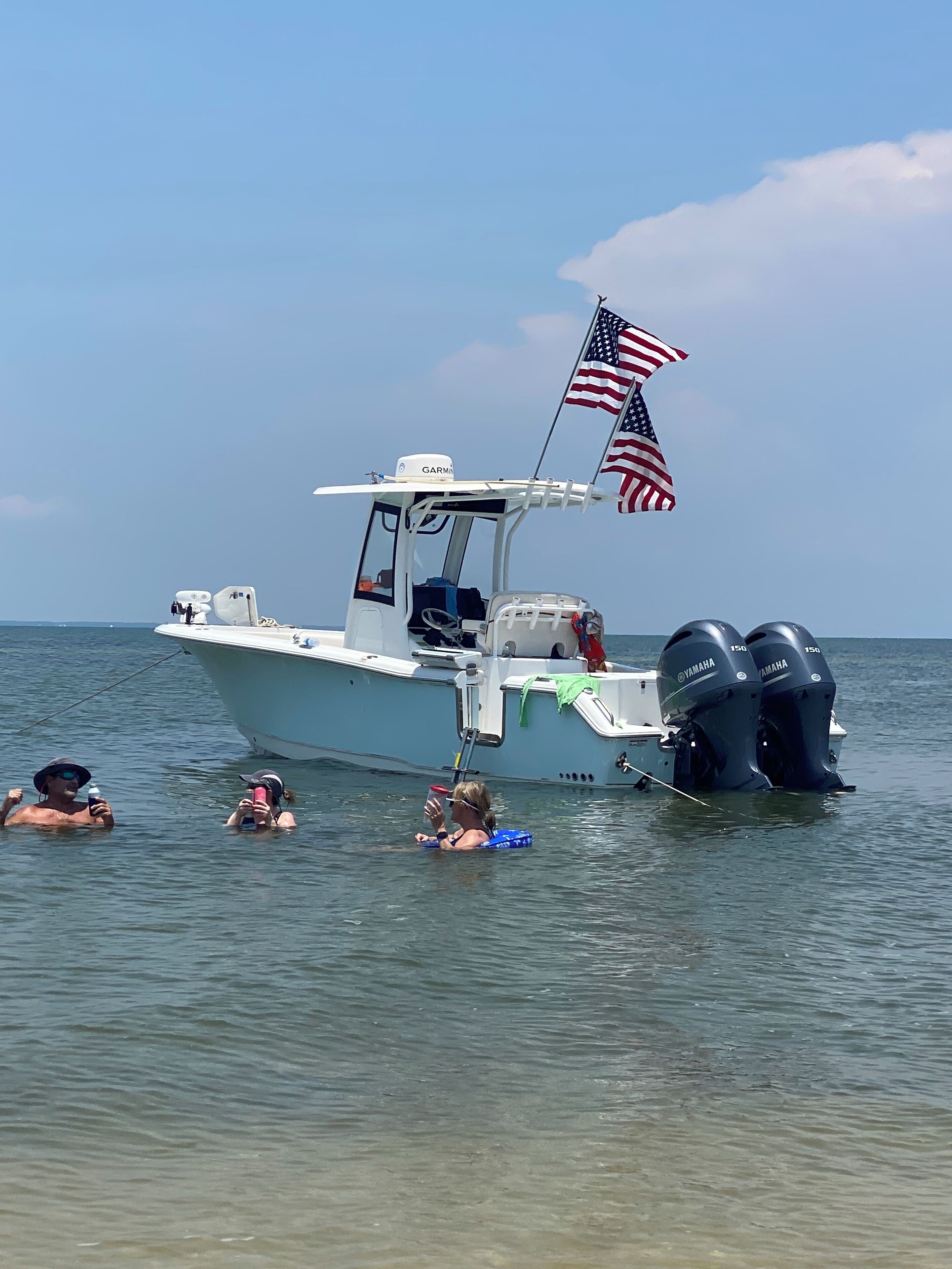 Un bateau arborant le drapeau américain, deux personnes qui nagent et un ciel dégagé.