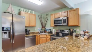 A kitchen with granite countertops, stainless steel appliances, wooden cabinets, and a 'BEACH' sign on the wall. - Luxurious King bed Condo across from Beach, Boardwalk, Shops and Restaurants.  (Biloxi)
