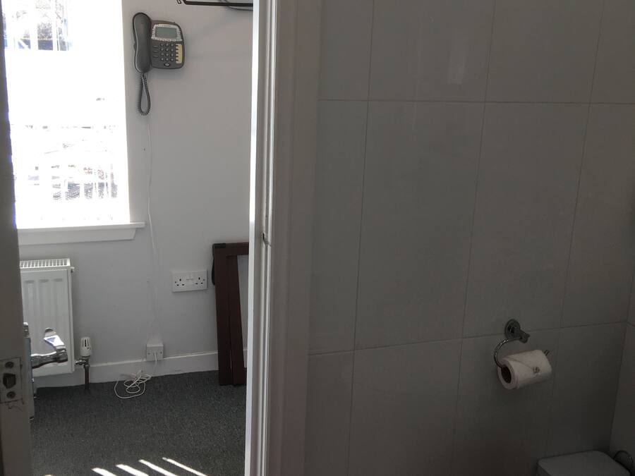 A bathroom with a toilet, a towel rack, a radiator, and a window.