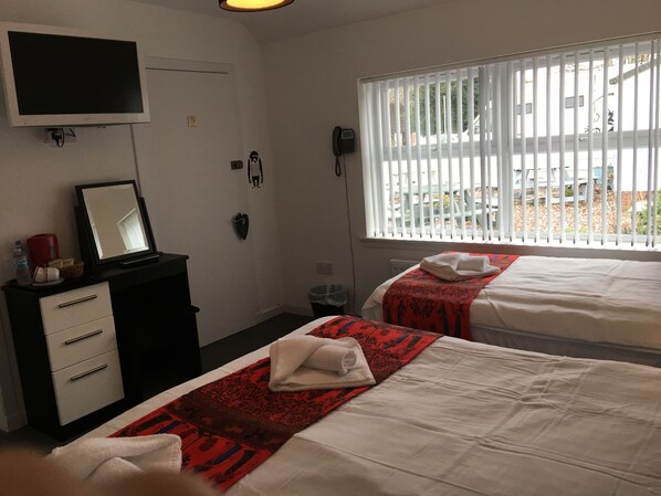 A hotel room with two beds, a desk with a mirror, a telephone, and a window with blinds.
