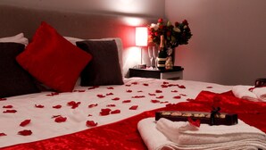 A hotel room with a neatly made bed, red and white bedding, a bouquet of flowers, and a bottle of champagne on the nightstand. - Comrie Hotel (Crieff)