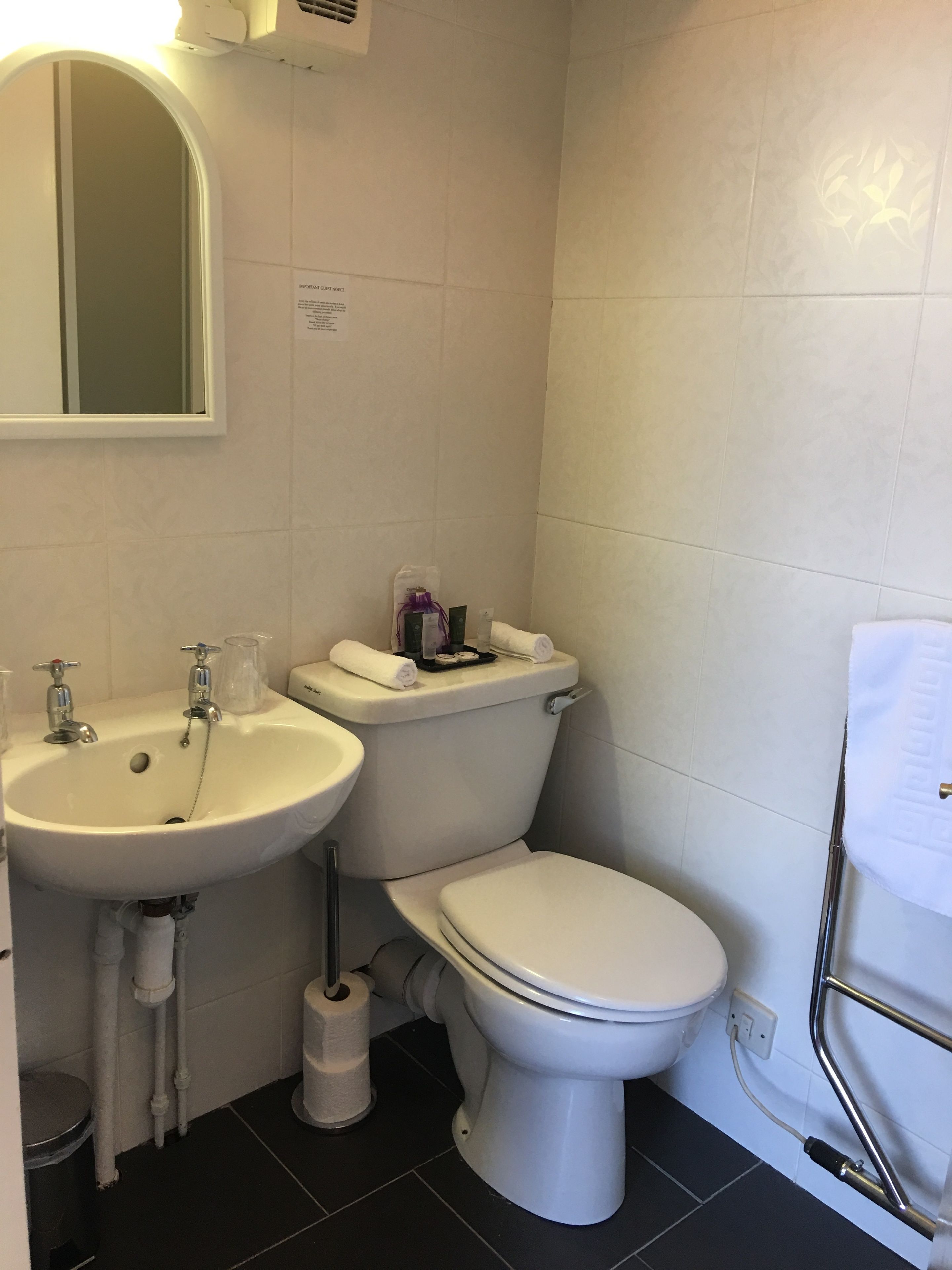 A small, clean bathroom with a white sink, toilet, and bidet. There is a mirror above the sink and a towel rack on the wall.