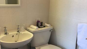 A small, clean bathroom with a white sink, toilet, and bidet. There is a mirror above the sink and a towel rack on the wall.