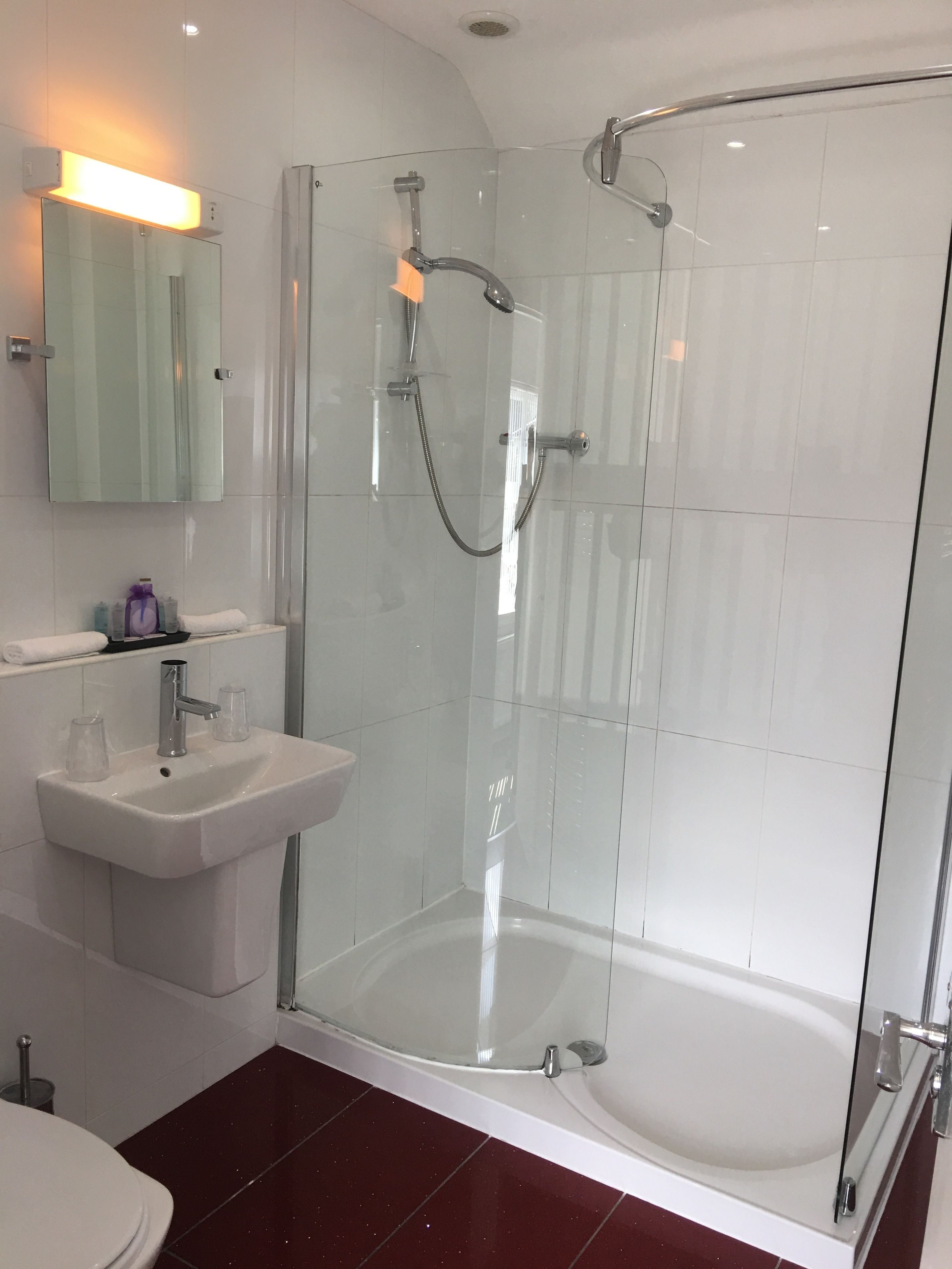 Un baño moderno con ducha de vidrio, lavamanos sobre pedestal y un inodoro.