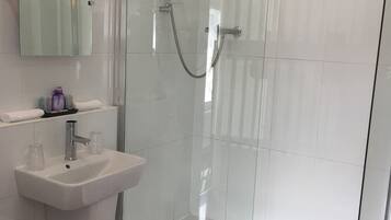 Un baño moderno con ducha de vidrio, lavamanos sobre pedestal y un inodoro.