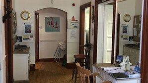 A hallway with a wooden floor, a desk with chairs, a chandelier, and a mirror. - Comrie Hotel (Crieff)