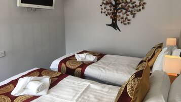 A hotel room with two beds, each with a white and maroon bedspread, and a decorative tree wall art.