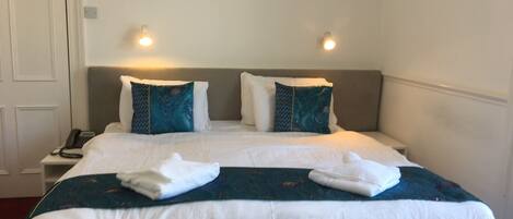 Habitación de hotel con una cama grande, dos almohadas, una mesita de noche con teléfono y una lámpara de pared.