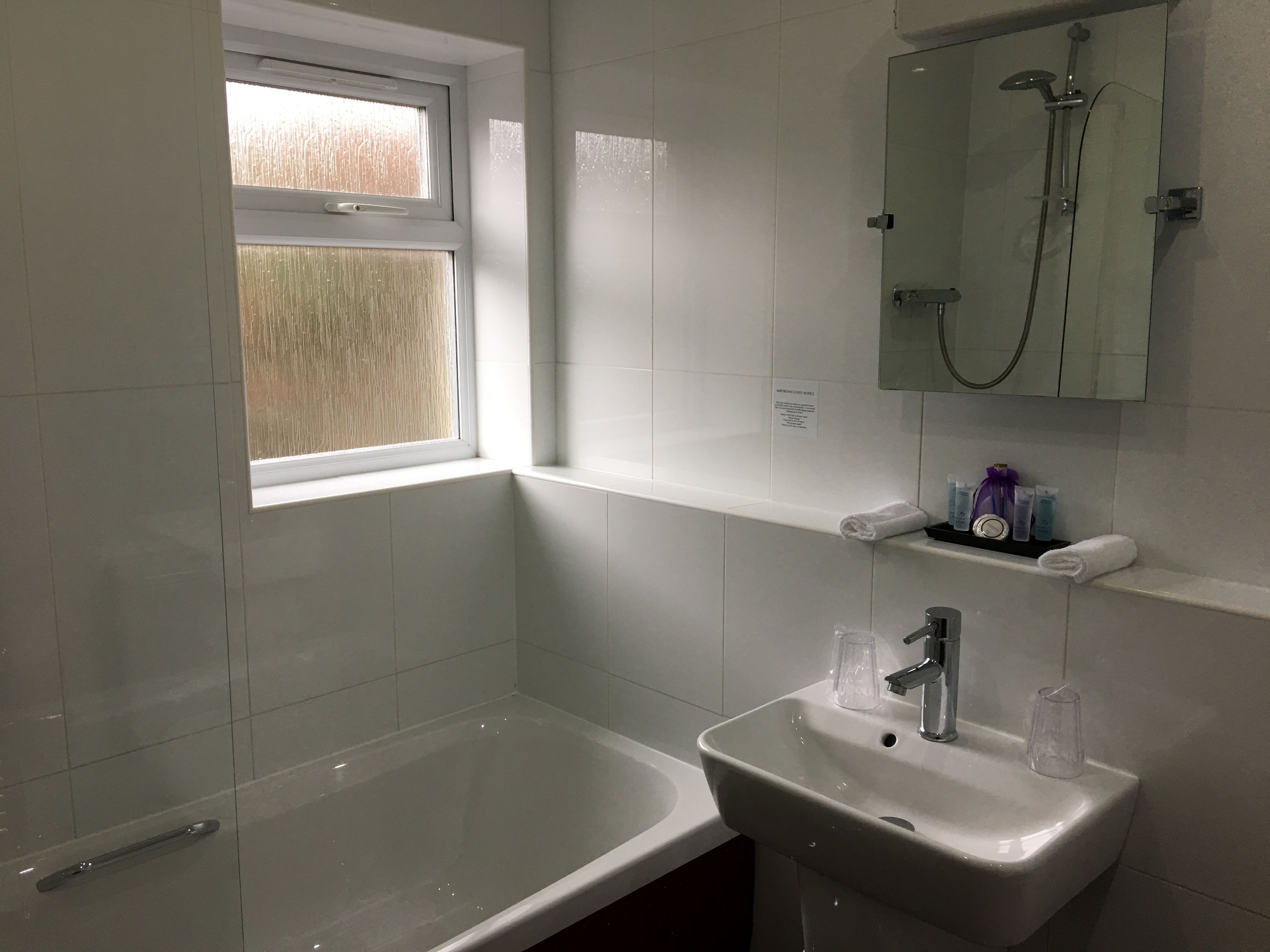 A bathroom with a bathtub, a sink, a window, and a shower.