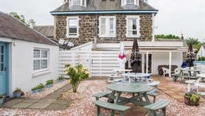 A stone building with a white exterior, a covered patio area with picnic tables, and a small shed to the left. - Comrie Hotel (Crieff)