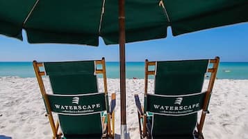 Two green Waterscape branded beach chairs under a green umbrella on a sandy beach.