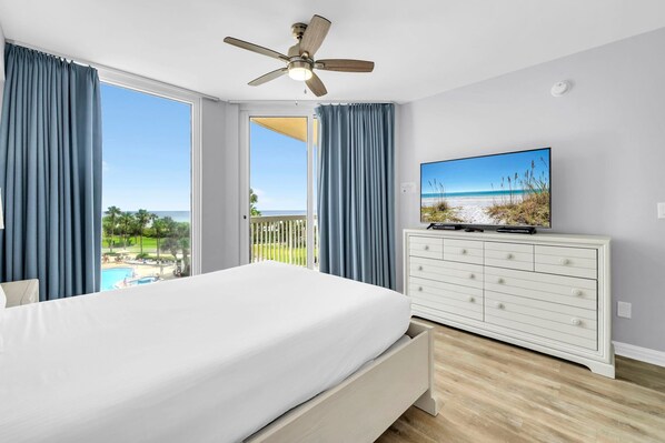 A bedroom with a bed, a ceiling fan, a TV on a dresser, and a view of the beach. - St. Maarten 402: Elegant 3BR Beachfront Condo in Silver Shells (Destin)
