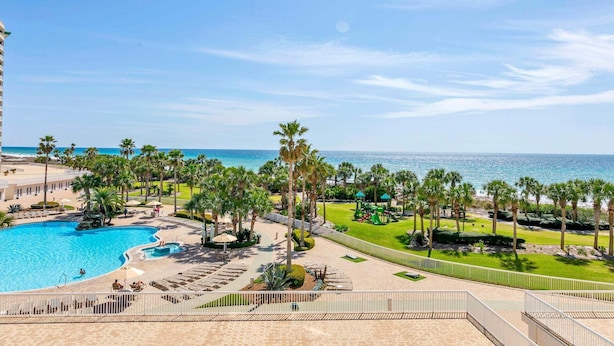 Um resort com piscina, palmeiras e vista para o oceano.