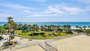 Um imóvel à beira-mar com um calçadão pavimentado, palmeiras e vista para o oceano.