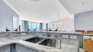 Cozinha moderna com uma ilha grande, pia de aço inoxidável e vista para o oceano através de amplas janelas.