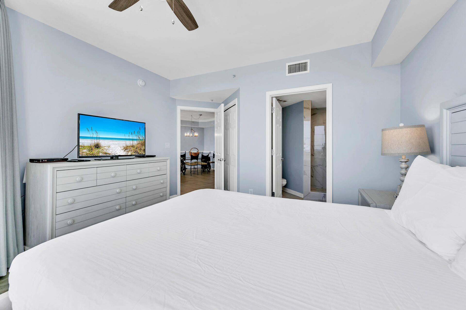 A hotel room with a large bed, a TV on a dresser, a ceiling fan, and a door leading to a bathroom.