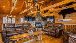 Ein rustikales Holzhaus-Interieur mit Ledersofas, einem Kamin aus Stein und einem Deckenventilator.