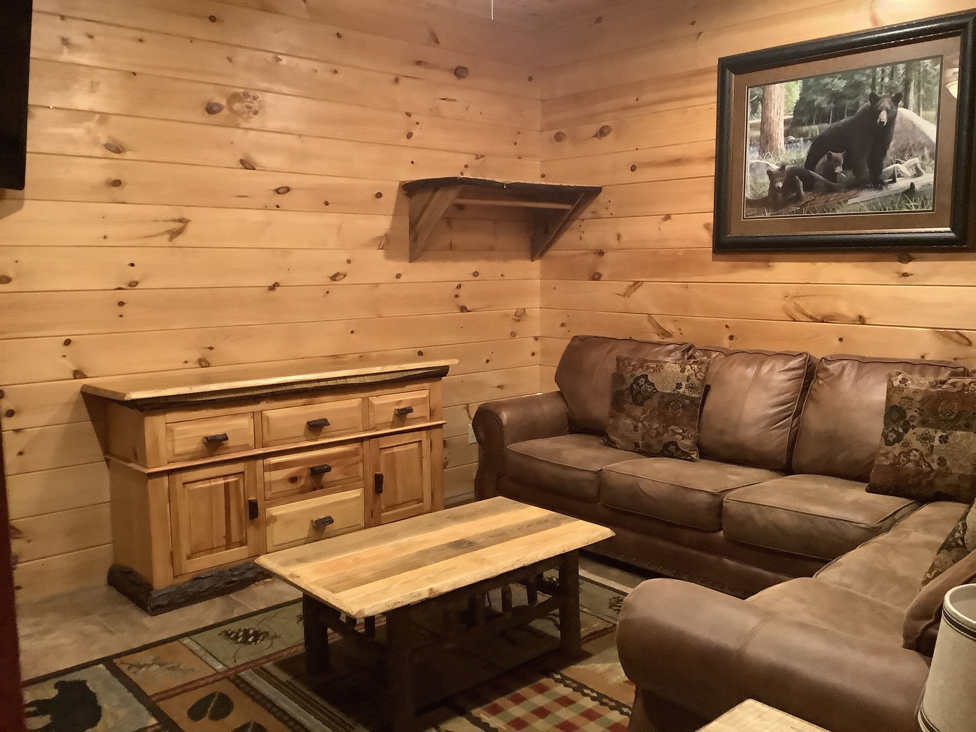 Una habitación acogedora con paredes de madera, un sofá de cuero marrón, una cómoda de madera y un cuadro con osos.