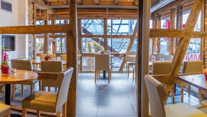 Un interior rústico con paredes de piedra, vigas de madera y un espacio central abierto con mesas y sillas.