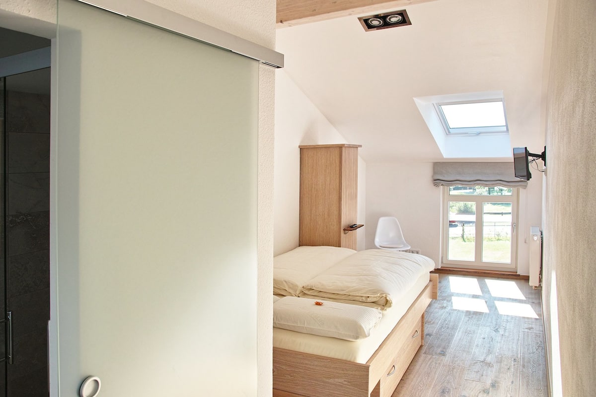 A bedroom with a skylight, a bed, a wooden wardrobe, and a view of the outdoors.