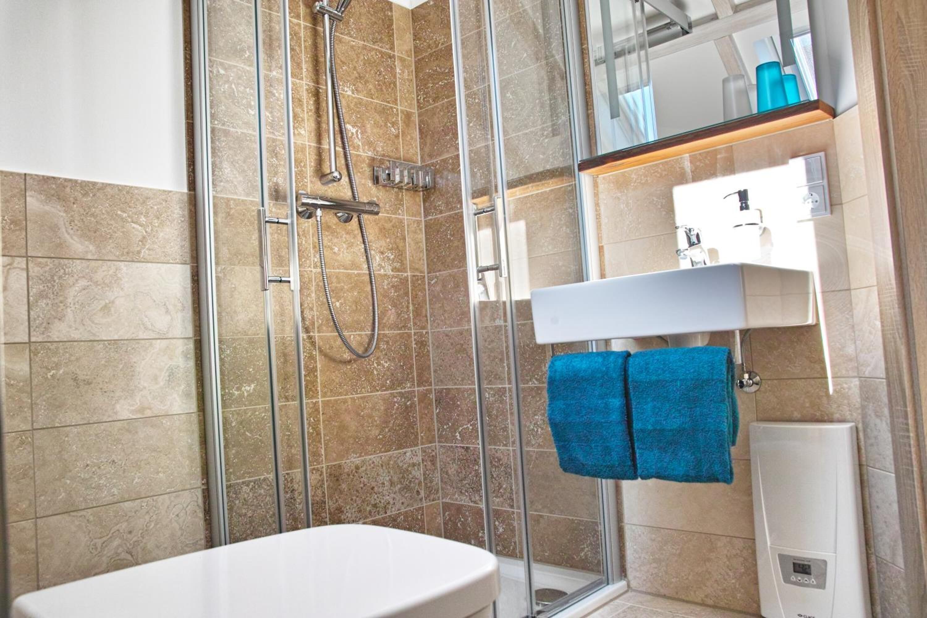 Un baño moderno con cabina de ducha de vidrio, un lavabo blanco y un perchero con toallas azules.