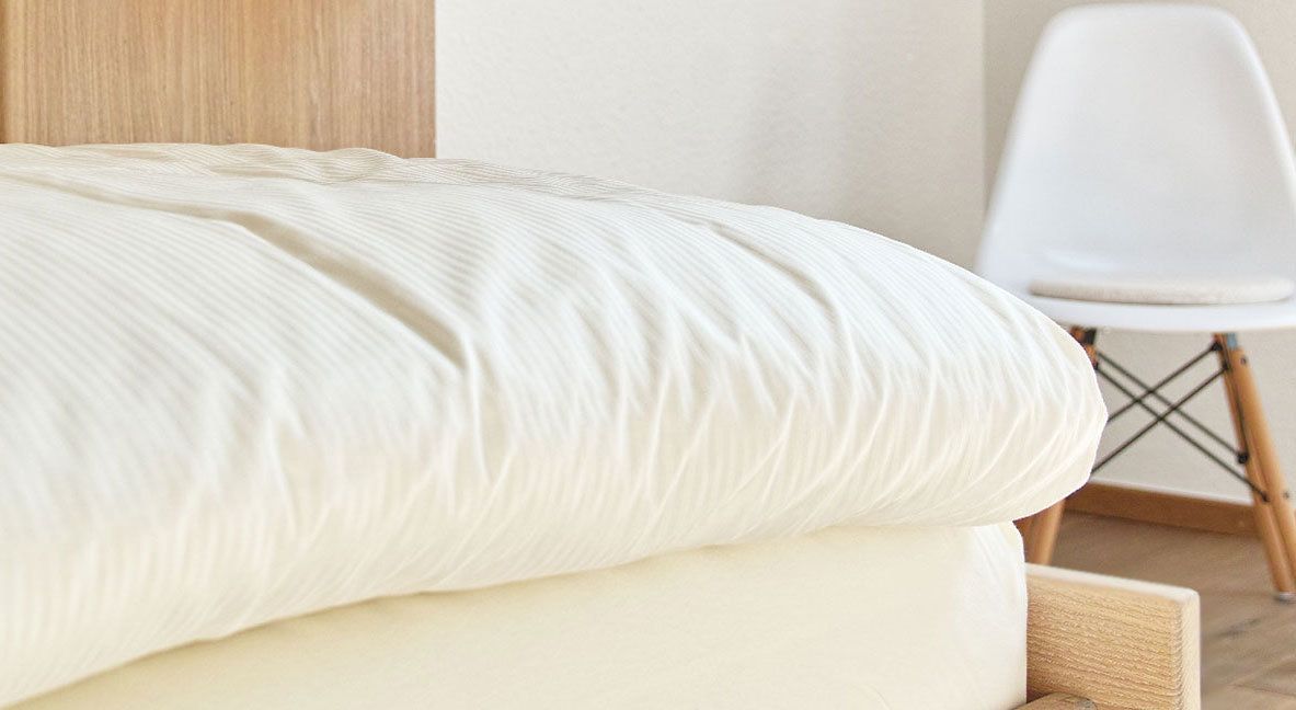 Uma cama com colchão e travesseiro brancos, num quarto com cabeceira de madeira e uma cadeira branca.