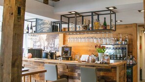 Zona de bar con vigas de madera, mostrador, taburetes y una variedad de botellas y vasos.