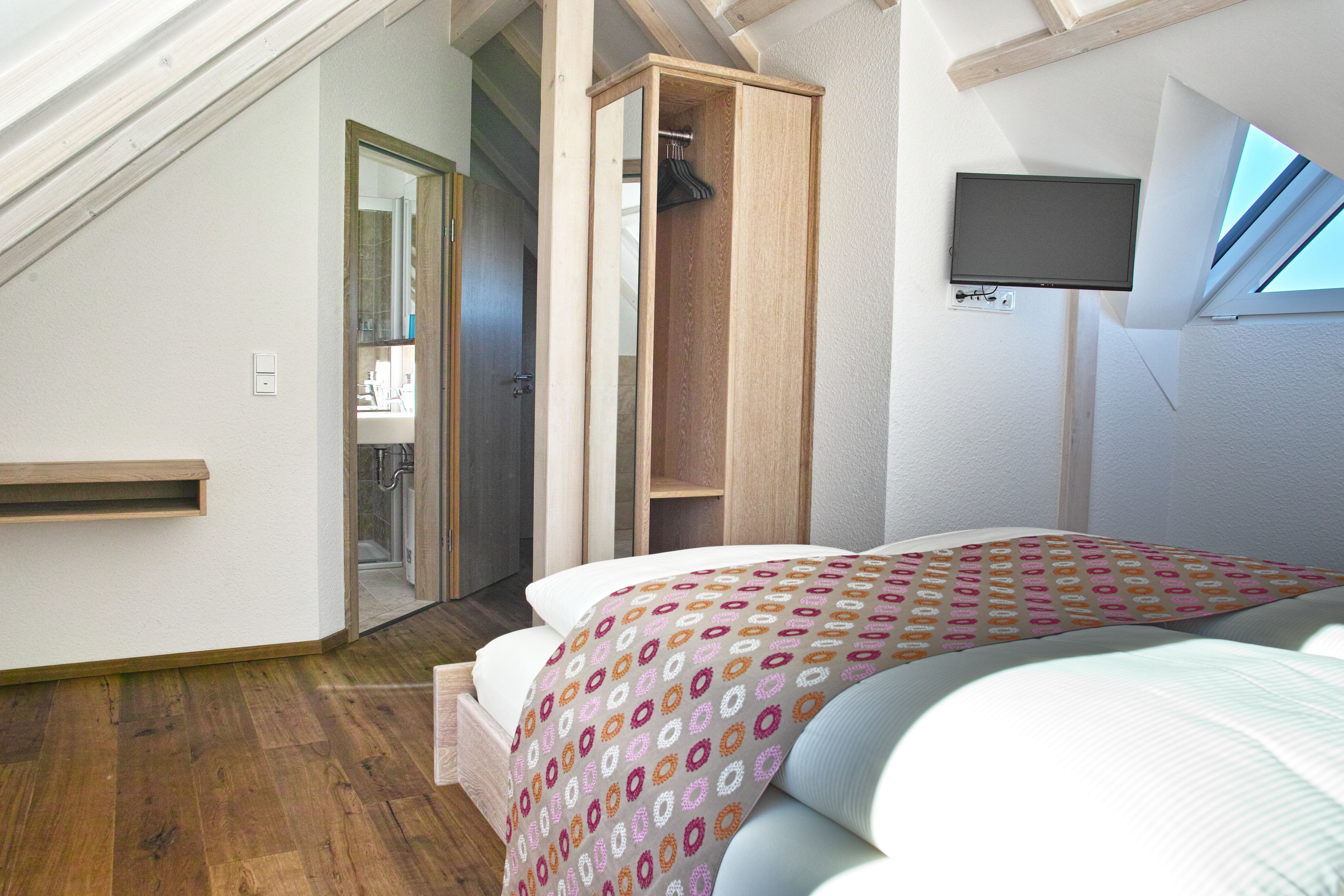 Un dormitorio con cama, armario de madera, televisor y tragaluz.