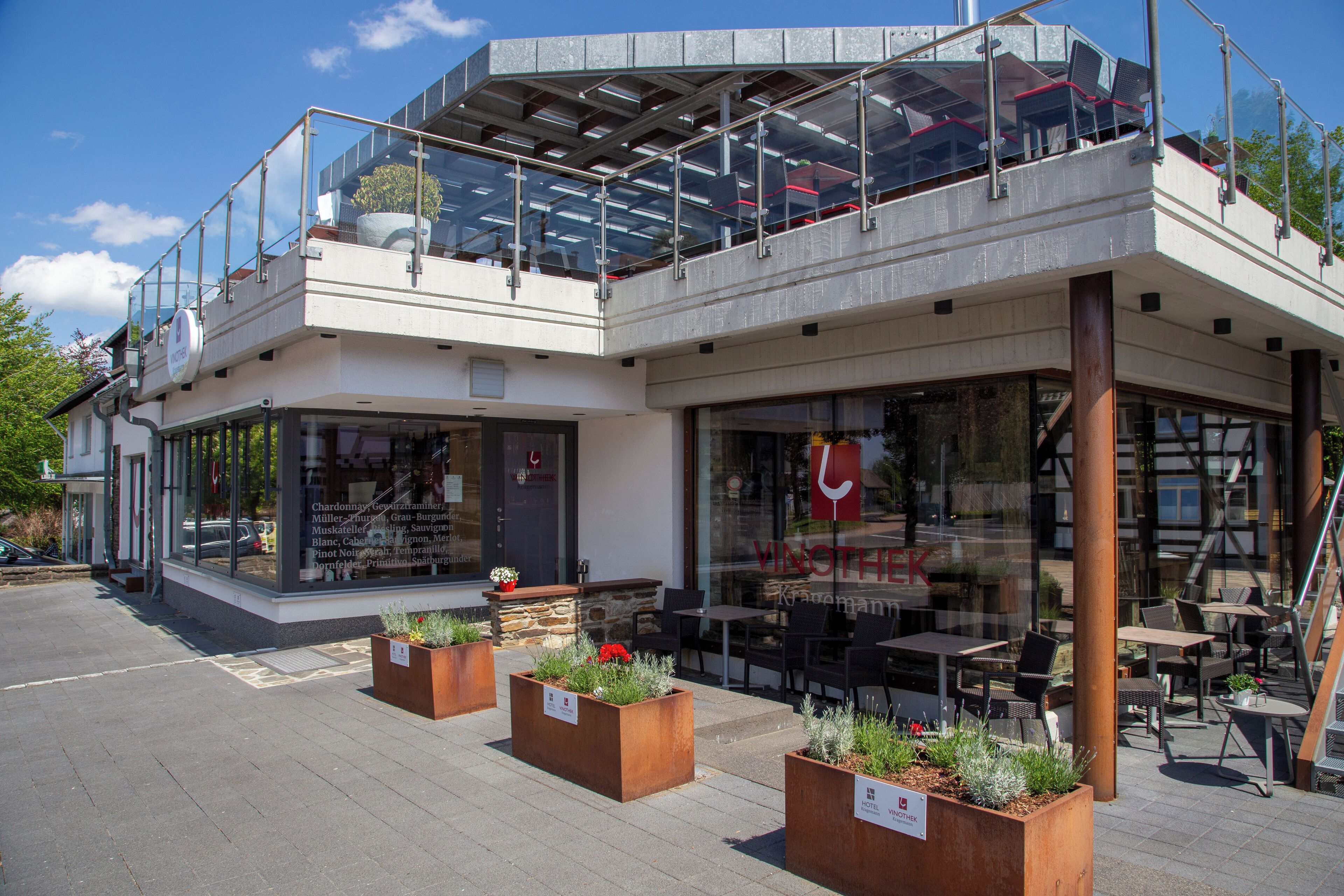 Een modern gebouw met een glazen gevel, een terras en een zichtbaar bord van een restaurant.