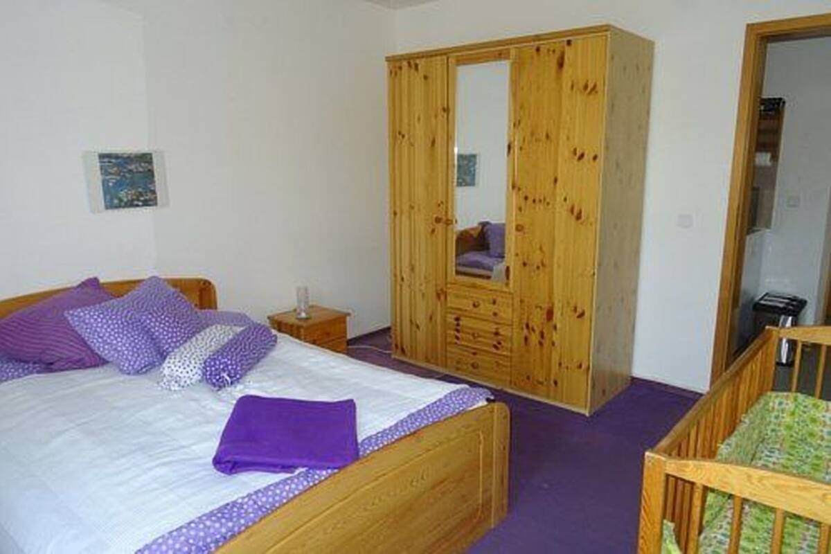 A bedroom with a bed, wooden wardrobe, and a crib.