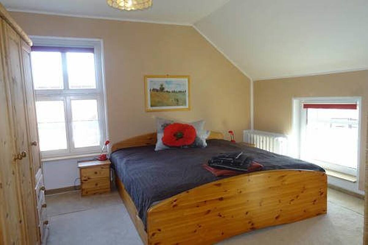 A bedroom with a wooden bed, a nightstand, a window, and a radiator.