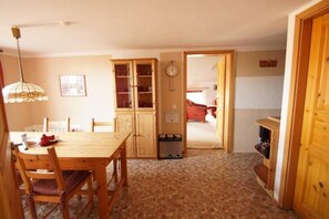 Un comedor con una mesa y sillas de madera, un aparador con puertas de cristal, un reloj en la pared y una puerta que da a otra habitación.