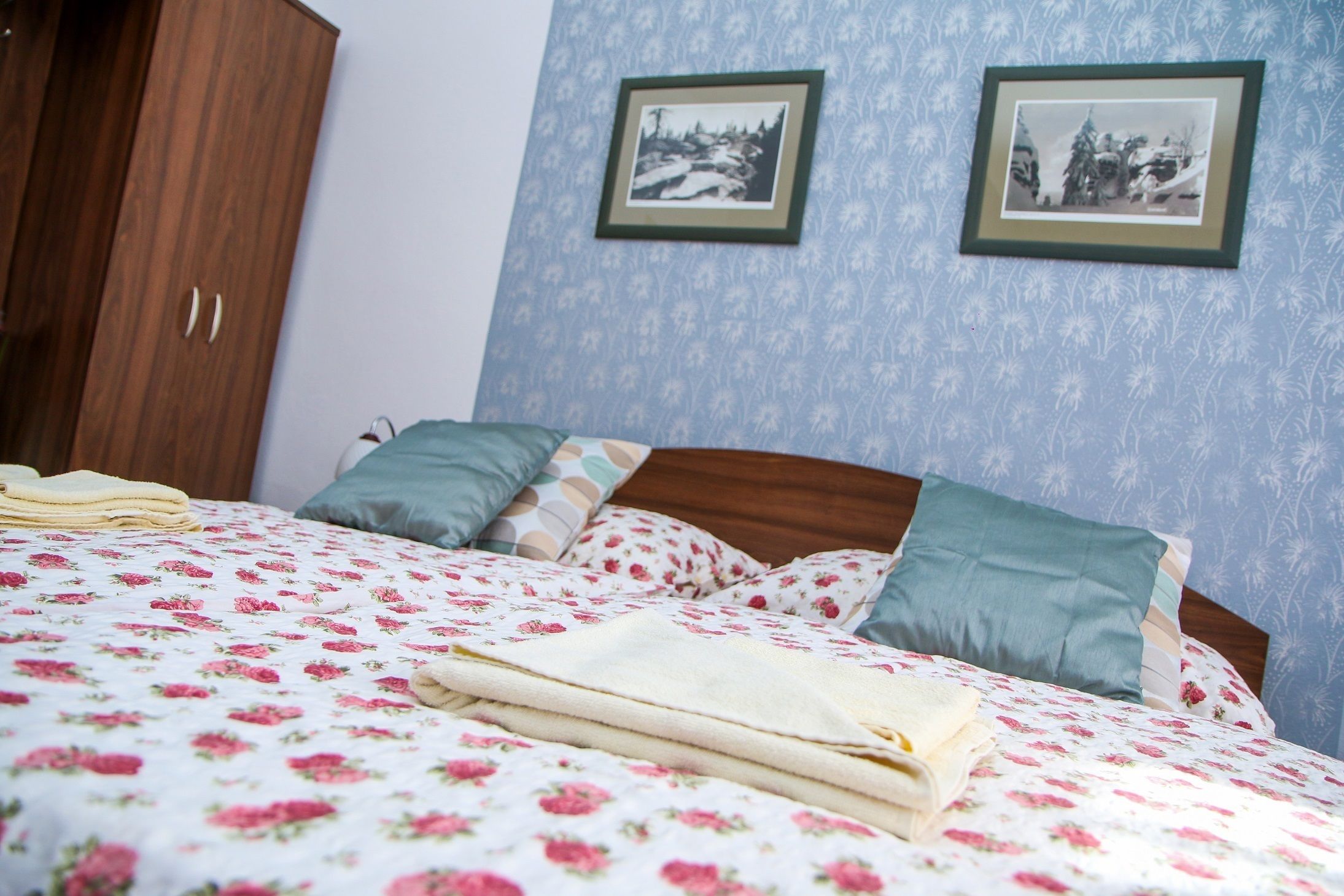 Una cama bien hecha con ropa de cama floral, un armario de madera y dos cuadros en la pared.