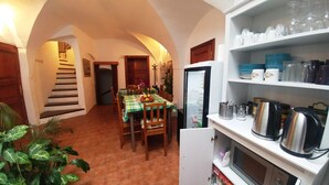 A kitchen with a dining table set for four, a refrigerator, and a microwave. There are plants and a staircase leading to another room. - Mini Hotel Abraka (Cesky Krumlov)