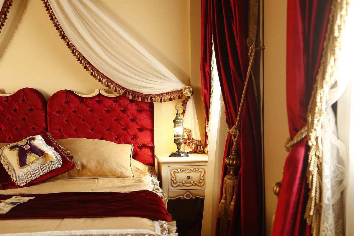 A four-poster bed with a canopy, red upholstered headboard, and a bedside table with a lamp.