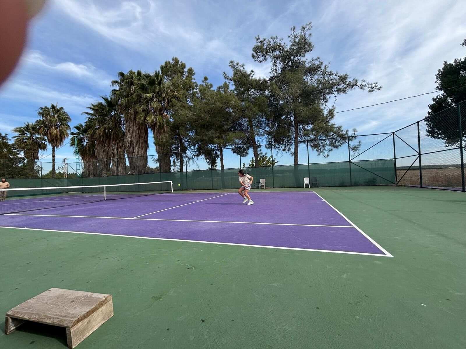 Cancha de tenis al aire libre con red, rodeada de árboles y un cielo despejado.