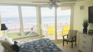 A bedroom with a large bed, a desk, and a chair, a balcony with a view of the ocean, and a ceiling fan. - #102 First Floor, Direct Ocean Front, 2 King Beds, 1 Queen Murphy, Dog Free 20# (Daytona Beach)