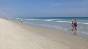 A beach with a wide sandy shore, a clear blue sky, and a few people walking along the water's edge. - #102 First Floor, Direct Ocean Front, 2 King Beds, 1 Queen Murphy, Dog Free 20# (Daytona Beach)