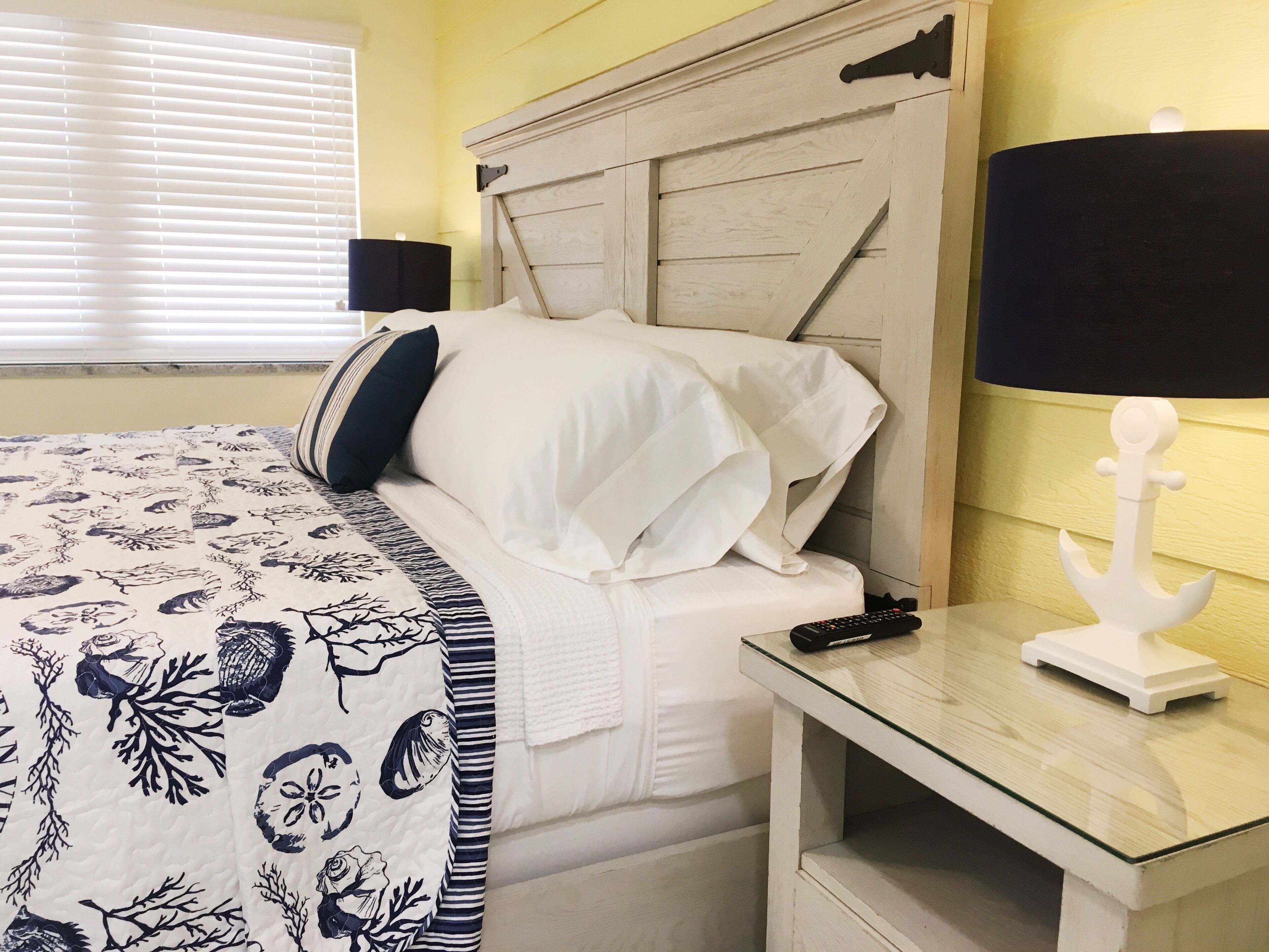 A bedroom with a bed, bedside table, lamp, and window with blinds.