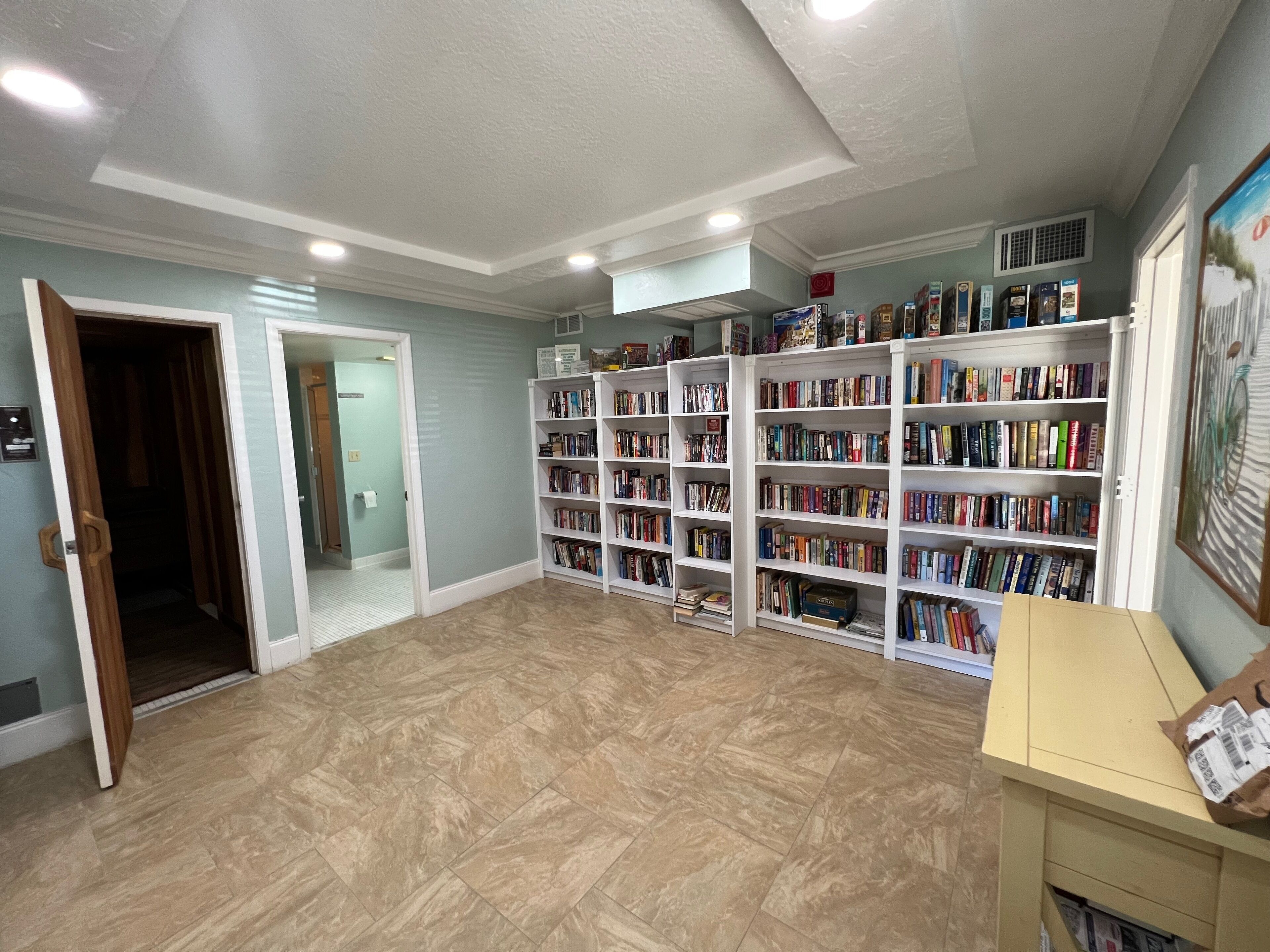 A spacious room with a large bookshelf filled with books, a wooden door, and a tiled floor.