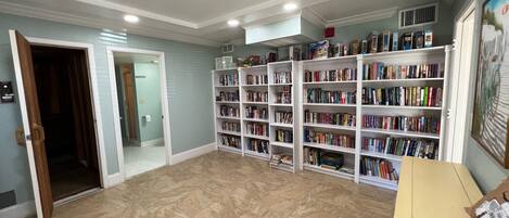 A spacious room with a large bookshelf filled with books, a wooden door, and a tiled floor.
