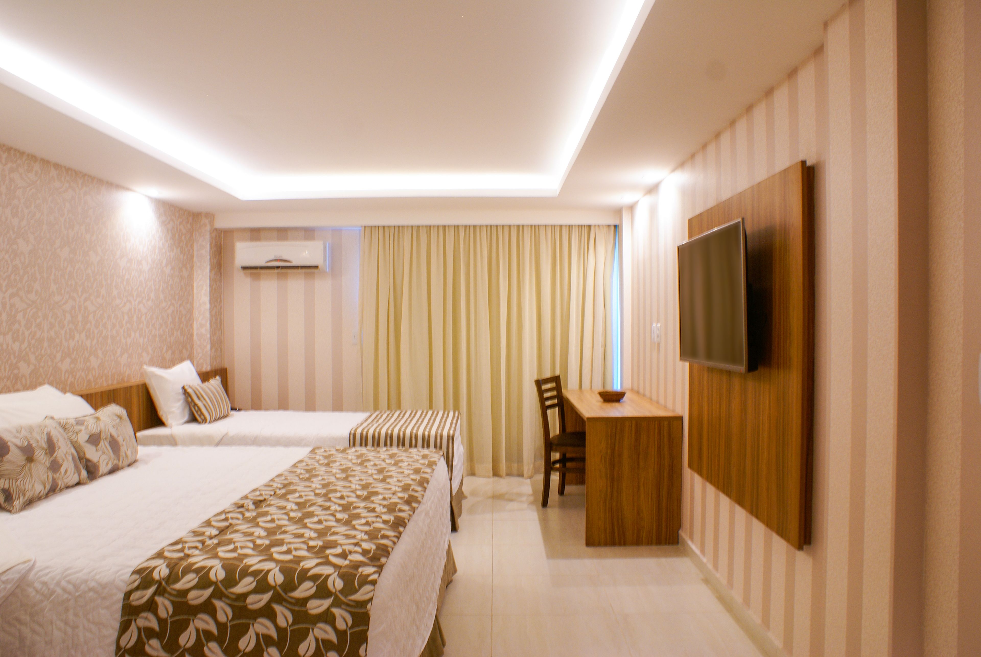 A hotel room with two beds, a desk, a chair, and a TV mounted on the wall.