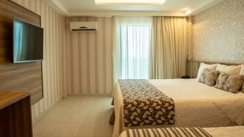 A hotel room with a large bed, a smaller bed, a TV mounted on the wall, and an air conditioning unit.