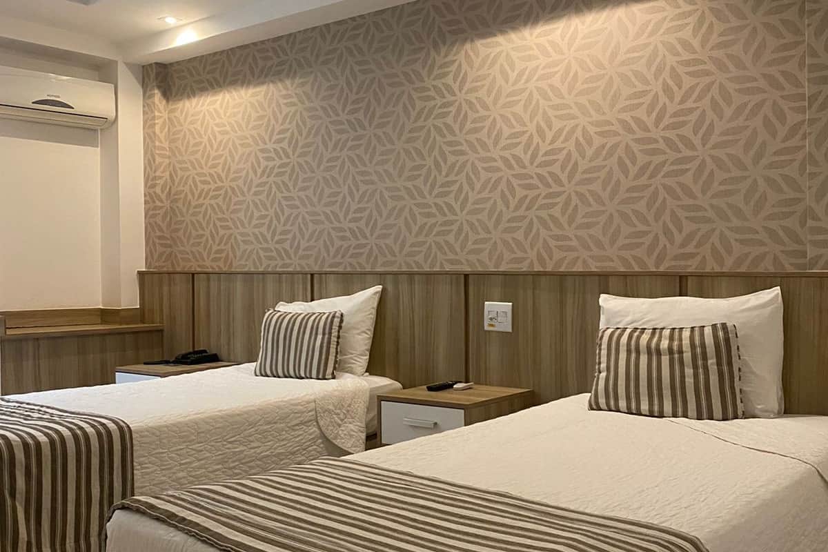 Ein Hotelzimmer mit zwei Betten, einem Holzkopfstück, einer Wand mit Muster und einer Deckenleuchte.