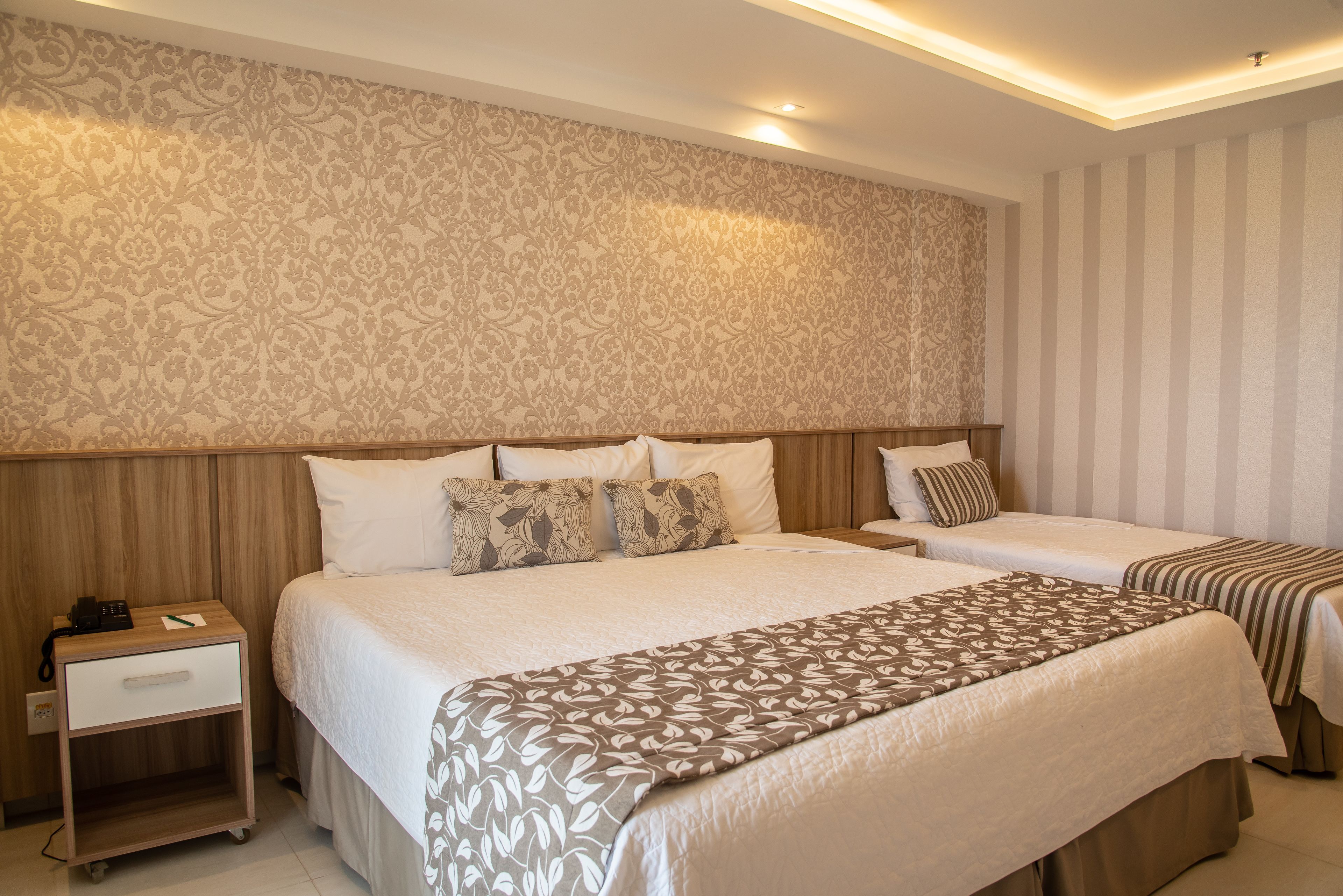 A hotel room with a large bed, a smaller bed, a nightstand, and a patterned wall.