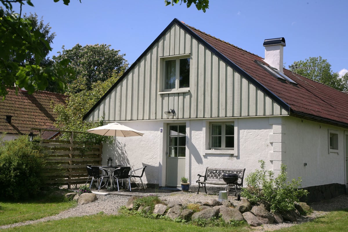 Et hvidt hus med skrå tag, skorsten og en lille veranda med et bord og stole.